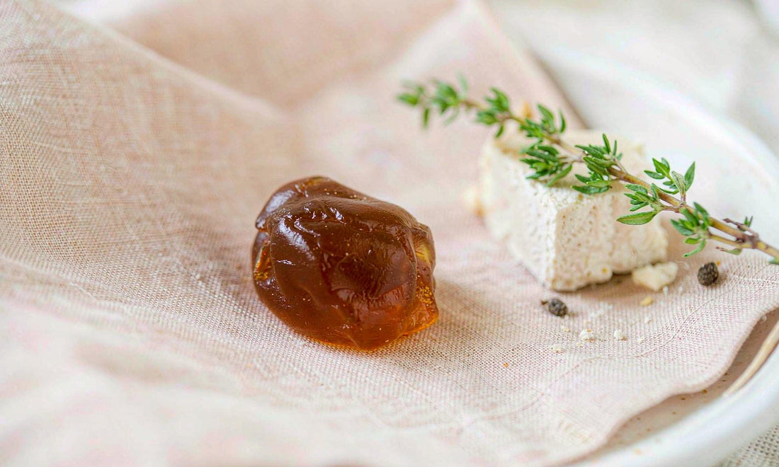 Macro close-up of an amber gummy on pale linen beside a wedge of aged cheese and a sprig of thyme