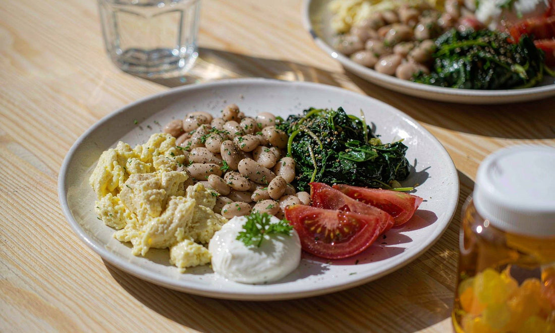Macro view of a plate with eggs, white beans, greens and tomato beside a tall glass of water