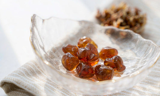 Macro view of amber gummies in a shallow glass dish on pale linen with dried granules behind