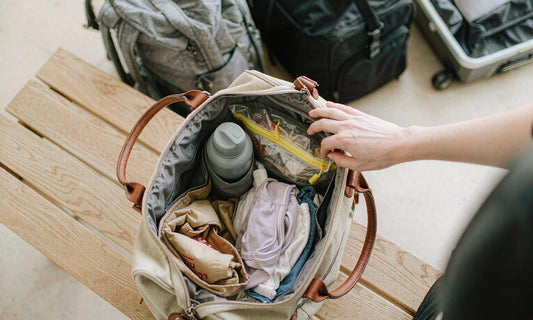 An open canvas travel bag packed with a water bottle, snack pouch and folded children's clothes