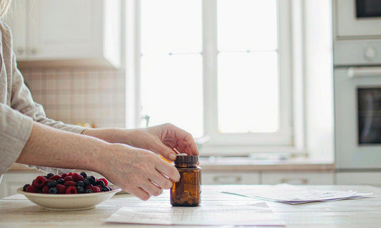 A pair of fair-skinned hands reading the label of an amber supplement jar on a bright family kitchen counter
