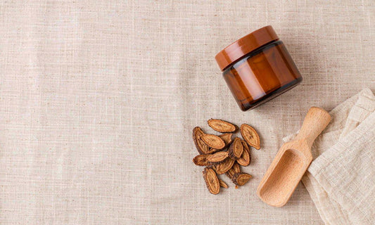 Overhead flat lay of dried sliced burdock root, a blank amber jar and a wooden scoop on pale linen