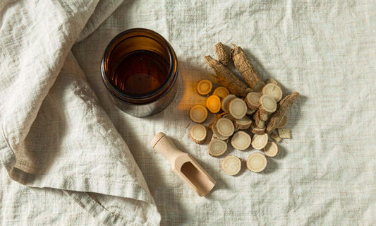 Overhead flat lay of dried sliced burdock root, a wooden scoop and a blank amber jar on pale natural linen