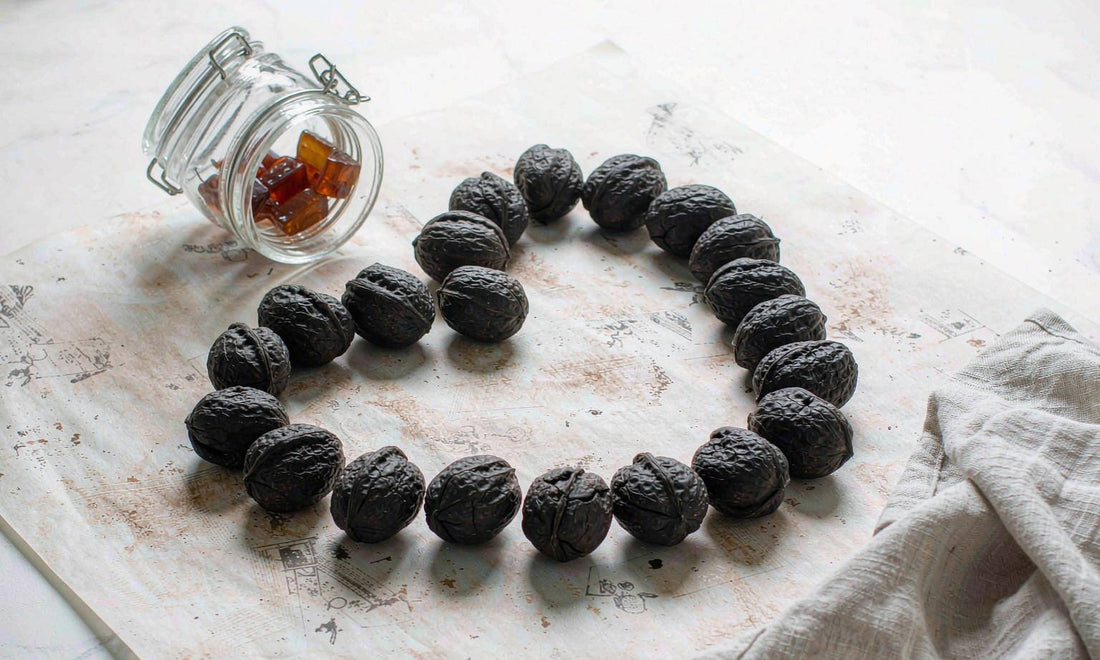 Flat lay of whole black walnuts in shell on butcher paper with an amber gummy jar on pale marble