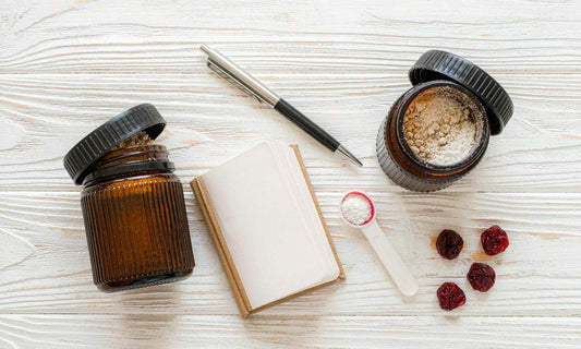 Overhead flat lay of two unlabeled amber jars, a blank notebook, pen, measuring spoon and dried berries