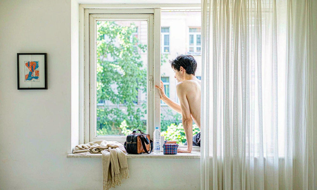 A travel bag, folded cardigan, water bottle and medication pouch on a bright hotel window sill