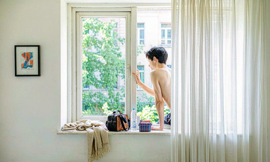 A travel bag, folded cardigan, water bottle and medication pouch on a bright hotel window sill