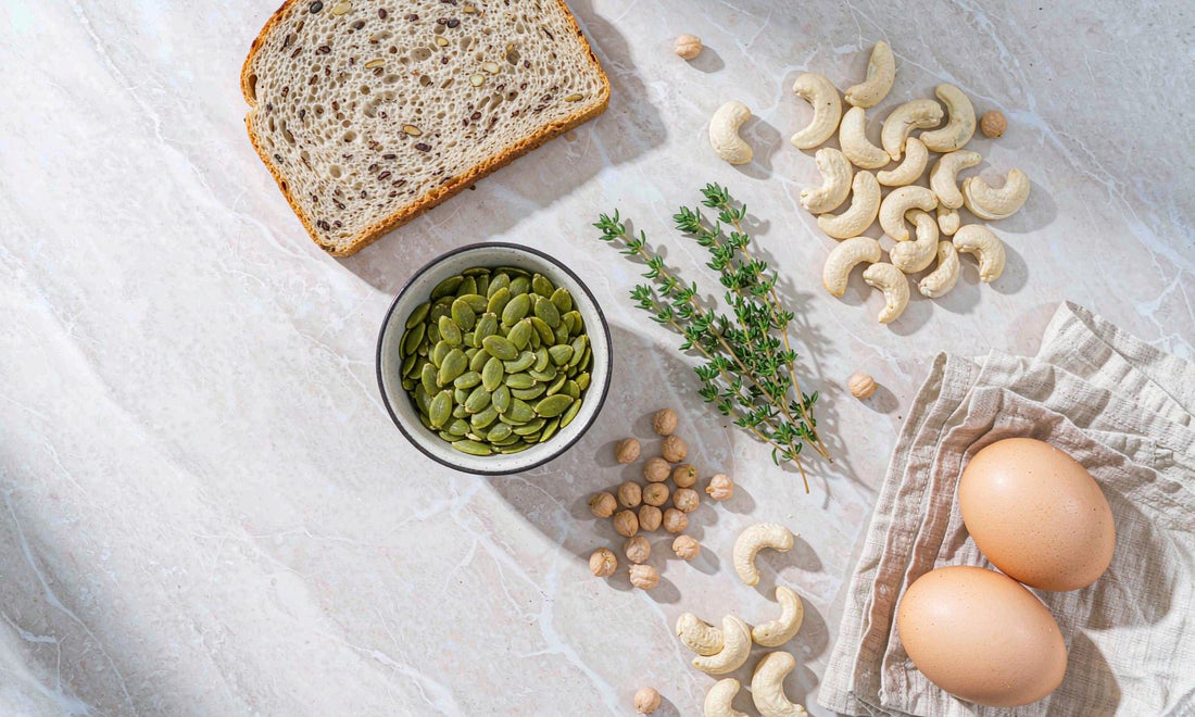 Overhead flat-lay of zinc-rich foods: pumpkin seeds, cashews, chickpeas and eggs on marble