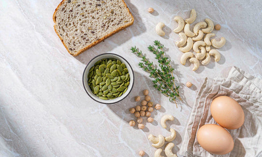Overhead flat-lay of zinc-rich foods: pumpkin seeds, cashews, chickpeas and eggs on marble