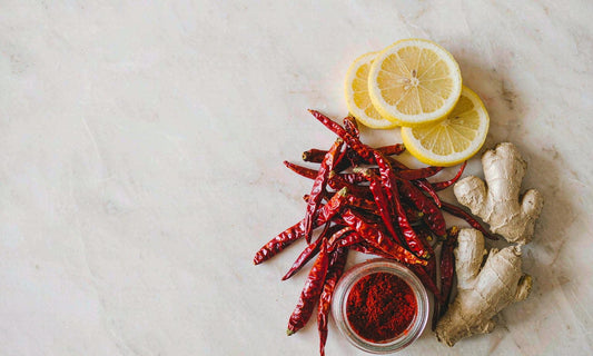 Dried red cayenne chili peppers arranged with lemon halves, ginger root and a glass jar on white marble