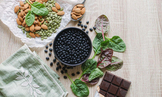 Overhead flat lay of almonds, pumpkin seeds, black beans, spinach leaves and dark chocolate on oak