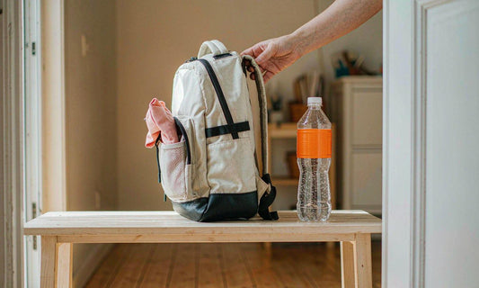A child's backpack and water bottle by the front door as an adult adjusts the strap at dawn