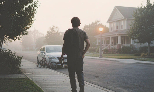 Commuter from behind with backpack and coffee cup walking toward golden sunrise light on a quiet street
